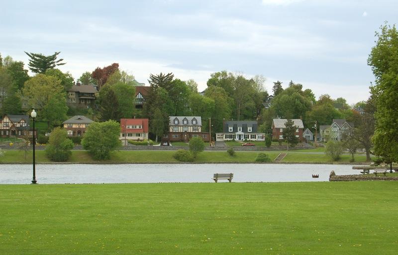 Green park lawn overlooking water with houses on a distant hill.