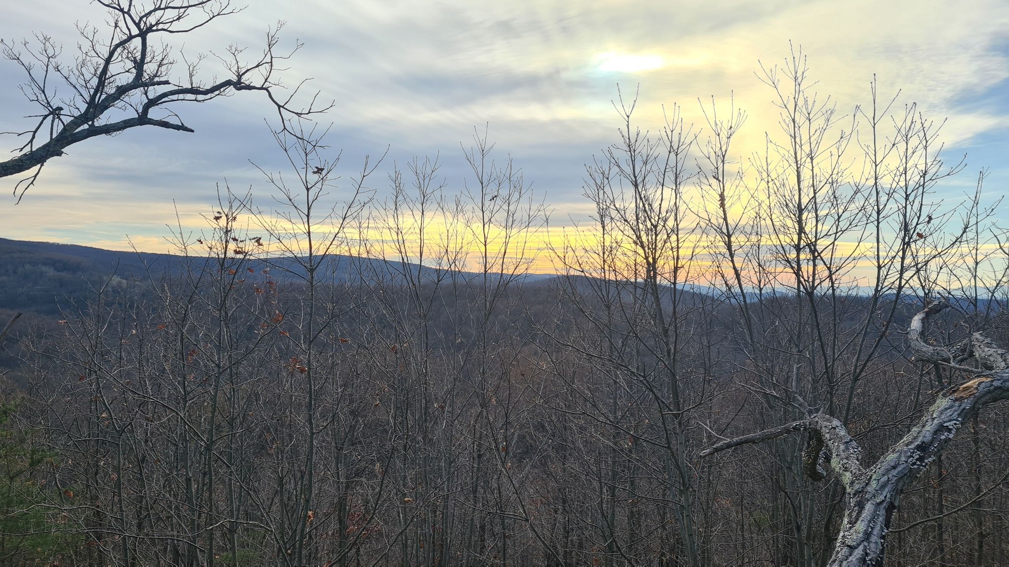 Bare trees frame a mountain landscape under a colorful sunset sky. - Buzzard Hill via Appalachian Trail