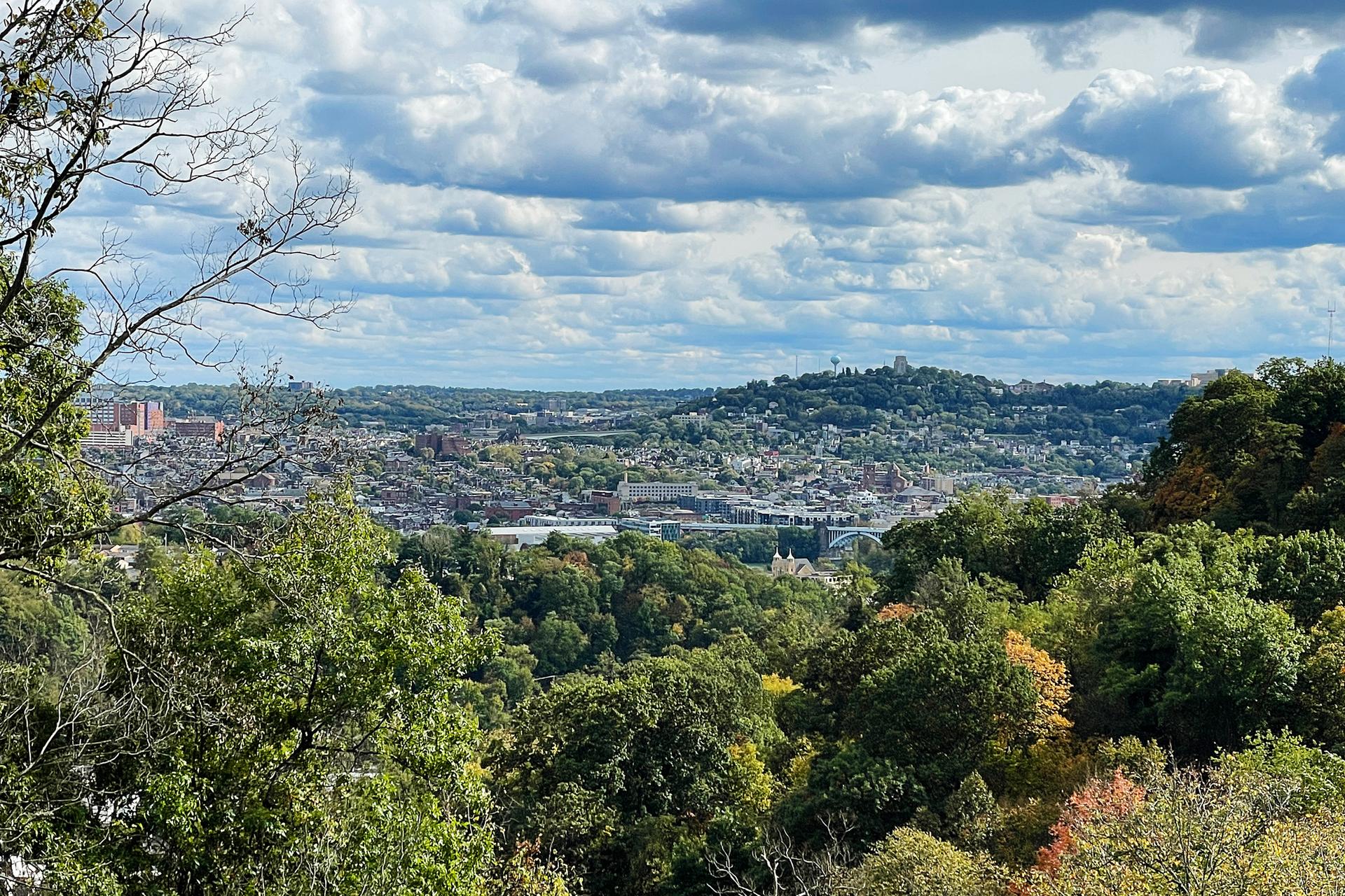 Panoramic view of a city surrounded by green hills under a cloudy sky.