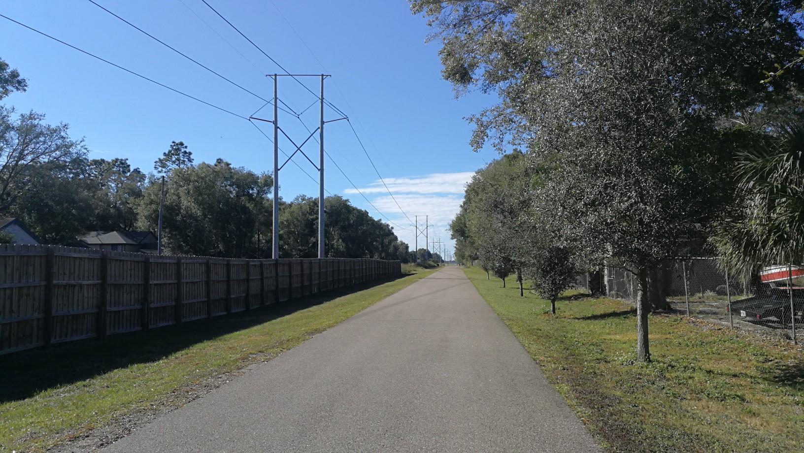 A long paved path runs alongside a wooden fence and power lines.