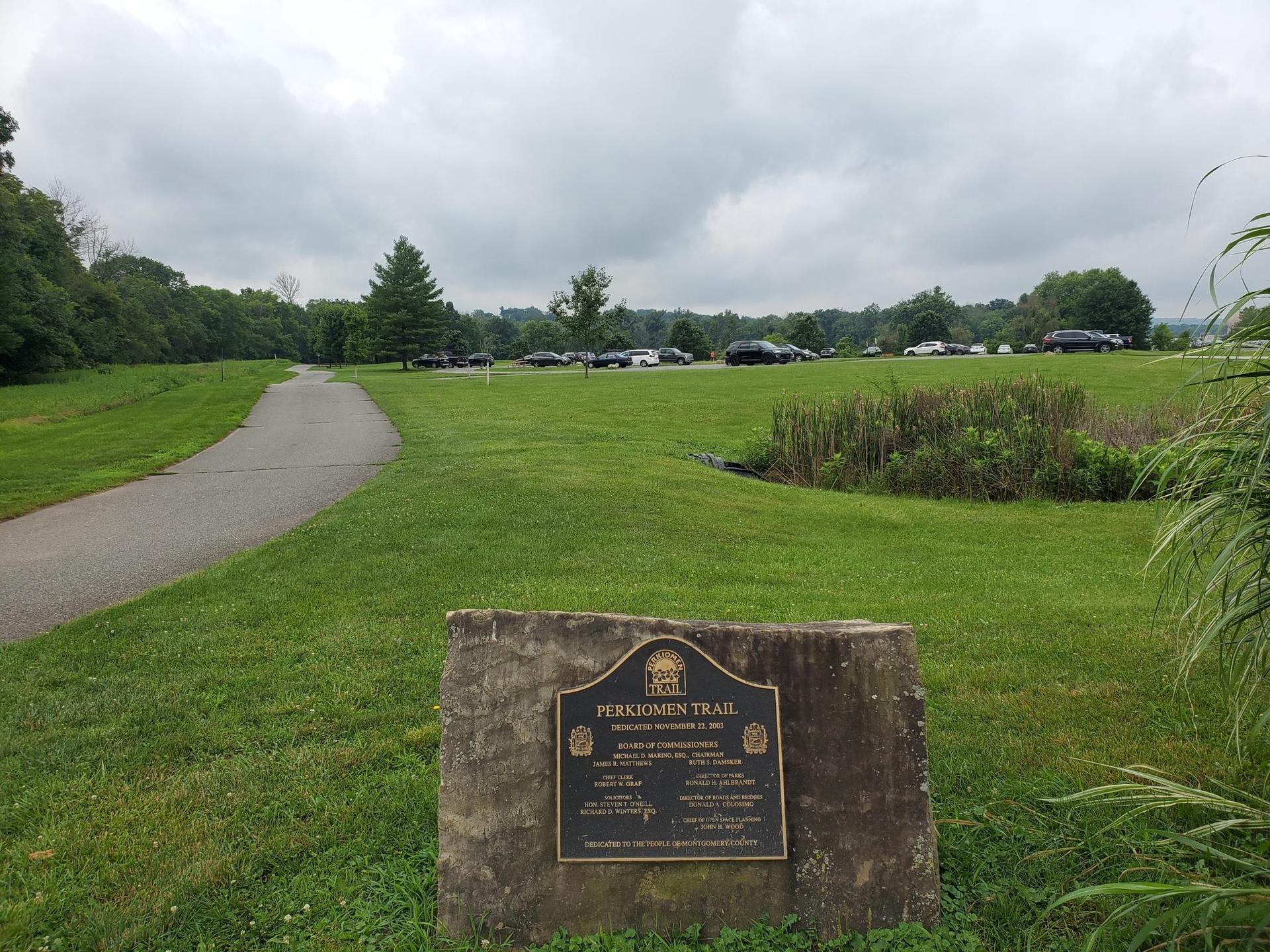 A paved path curves through a grassy field under a cloudy sky.