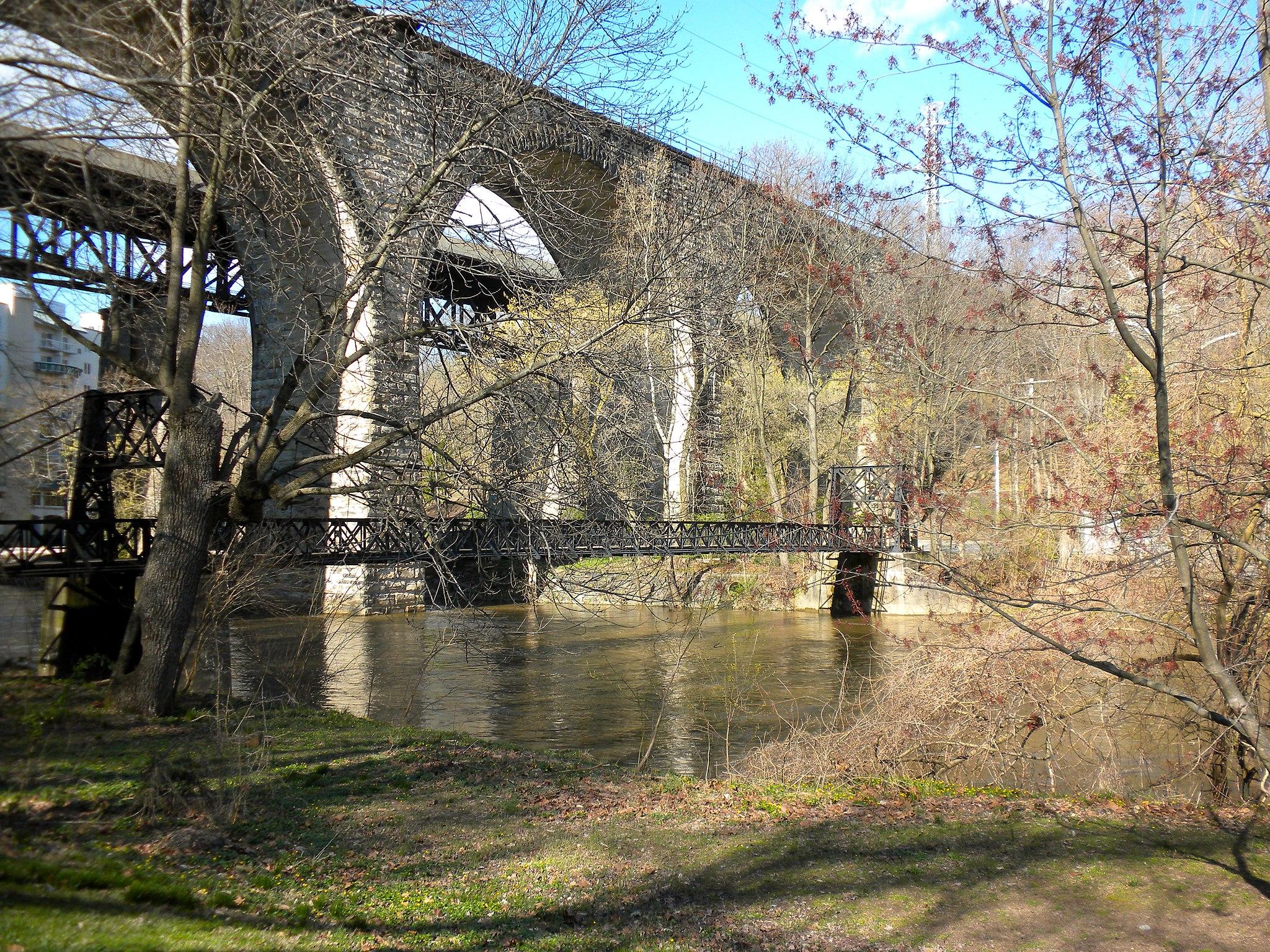 A large stone and metal bridge spans a river with bare trees.