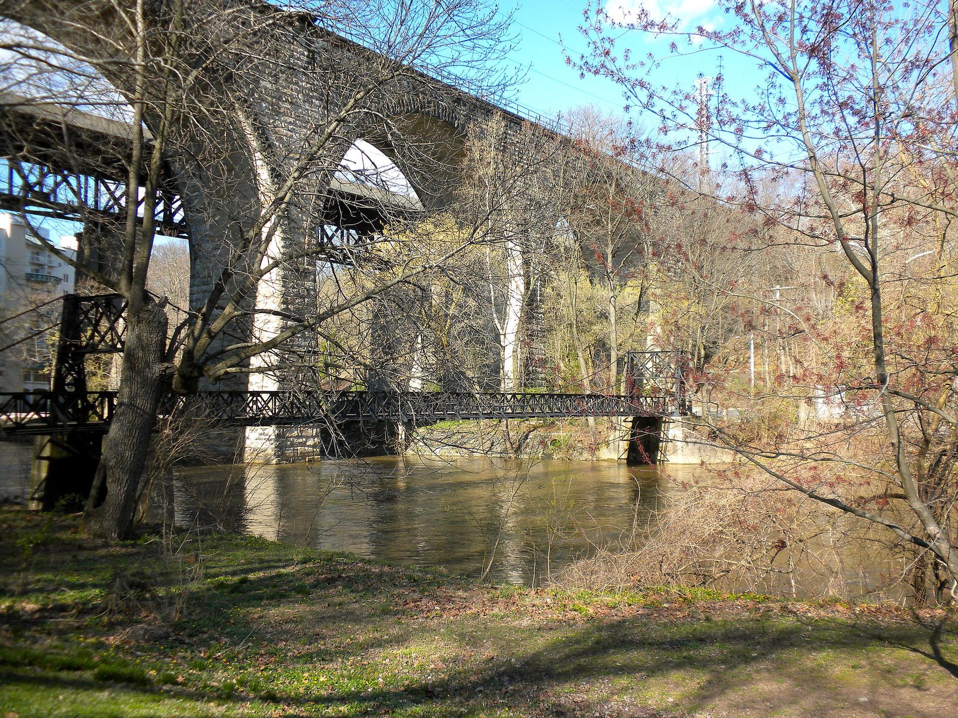 A large stone and metal bridge spans a river with bare trees.