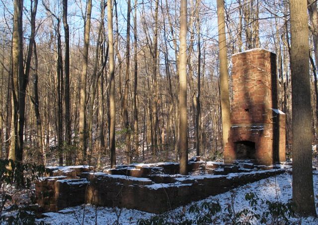 Old brick chimney and stone ruins in a snowy, sunlit forest. - Elders Run and Middle Creek Trail Loop