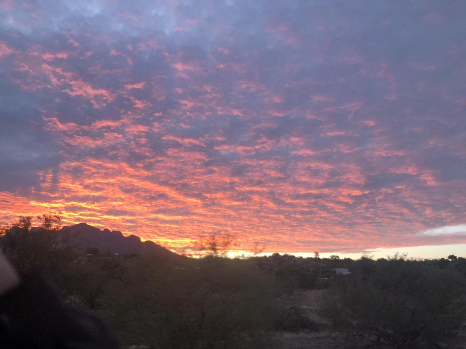 Vibrant orange and purple sunset clouds fill the sky over a dark desert horizon.