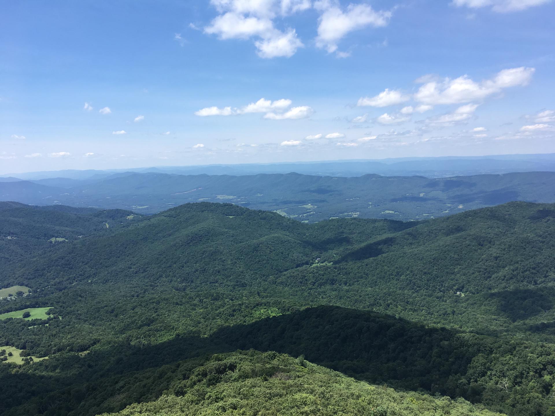 Vast green mountain range under a bright blue sky with white clouds.