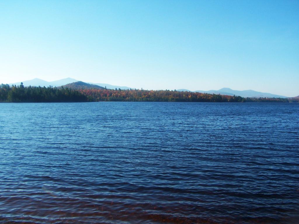 Wide view of a calm lake with a distant forested shore and mountains.