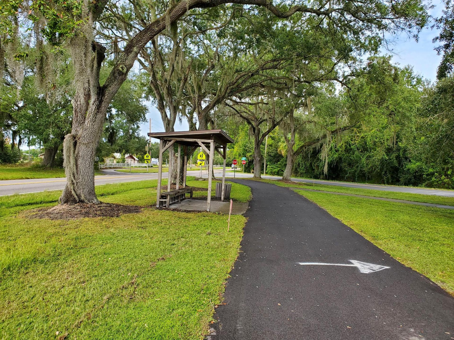 Paved path with arrow, wooden shelter, and large trees with moss.
