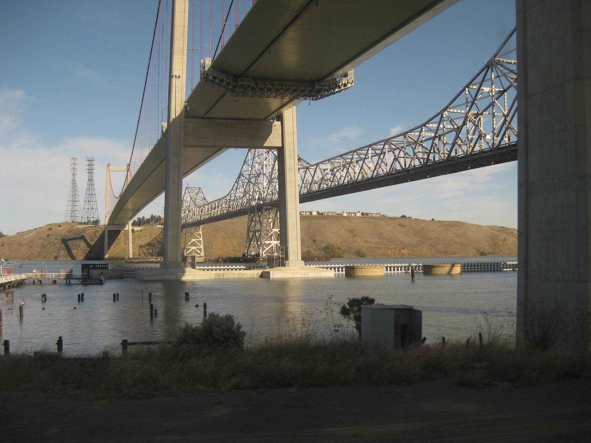 View beneath two large bridges spanning calm water and distant hills.