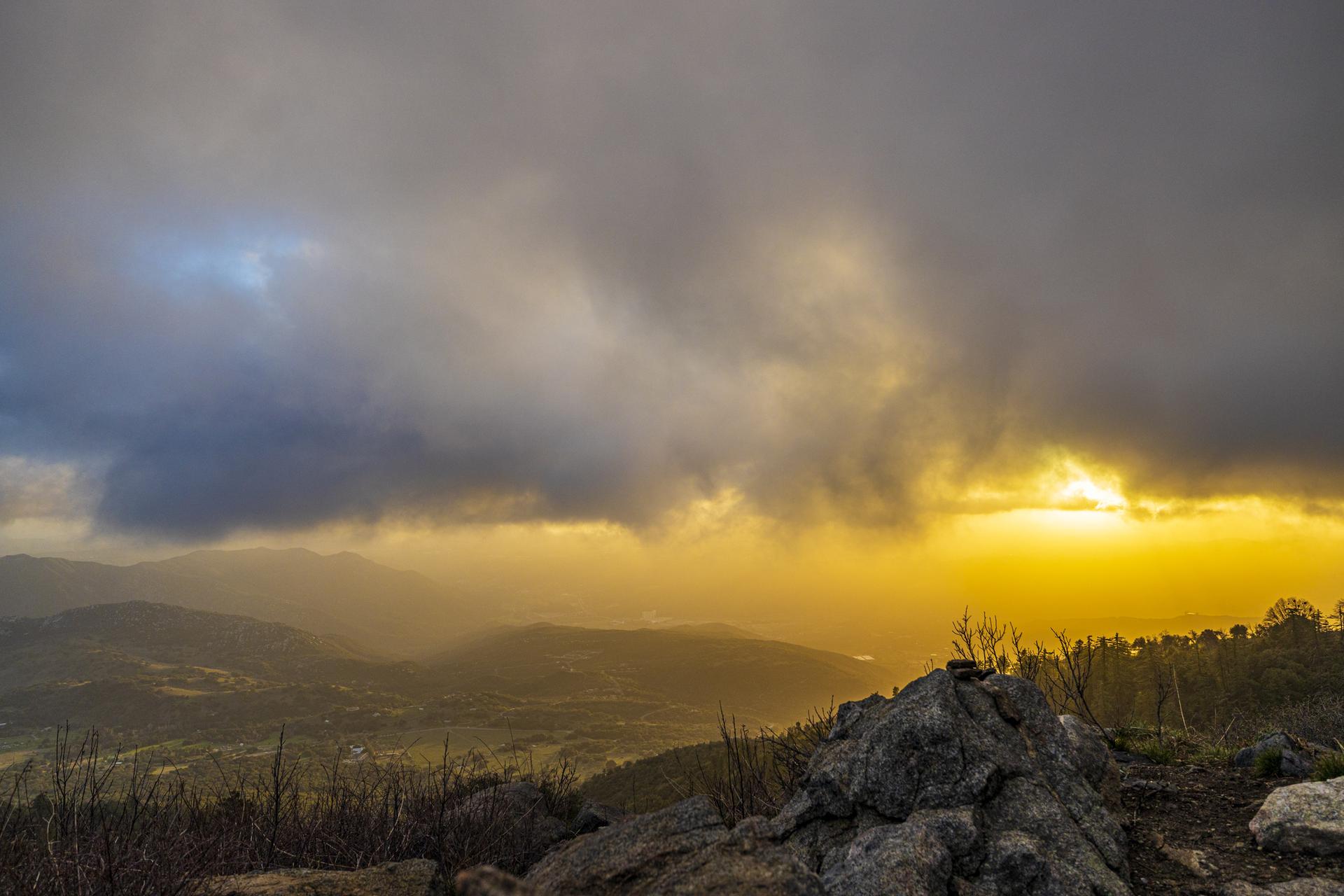 Golden sunset light illuminates distant mountains under a dramatic cloudy sky.