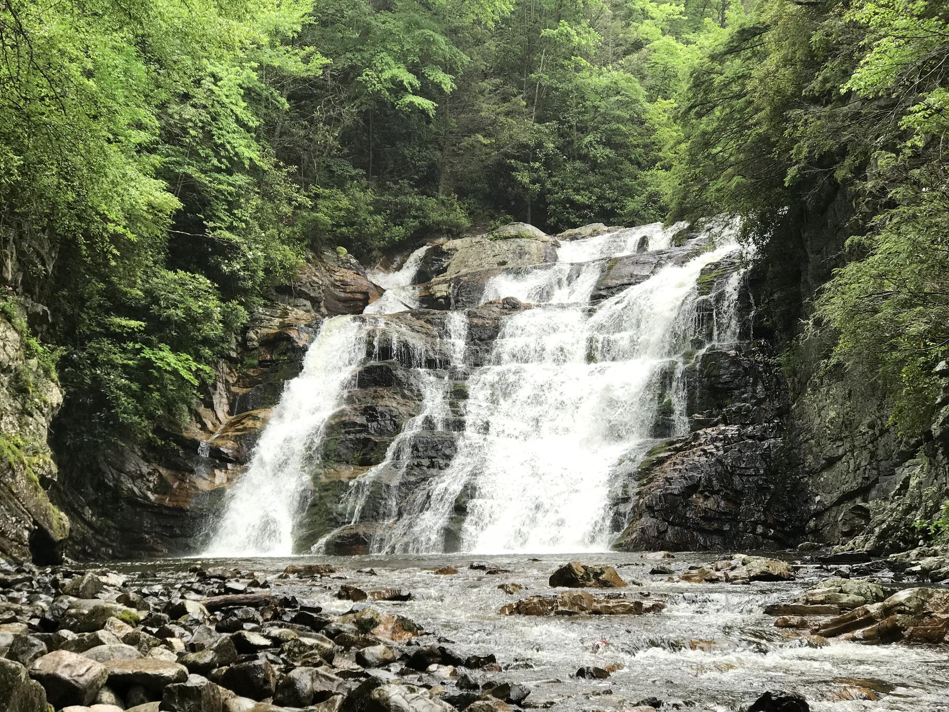 Multi-tiered waterfall cascading over dark rocks into a rocky river.