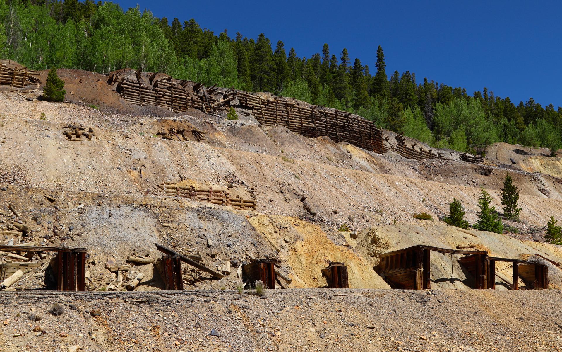 Terraced hillside with wooden support structures and small mine entrances under a blue sky.