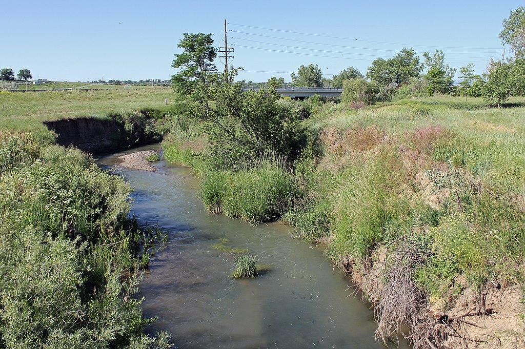 Narrow stream flowing through grassy banks under a bright, clear sky.
