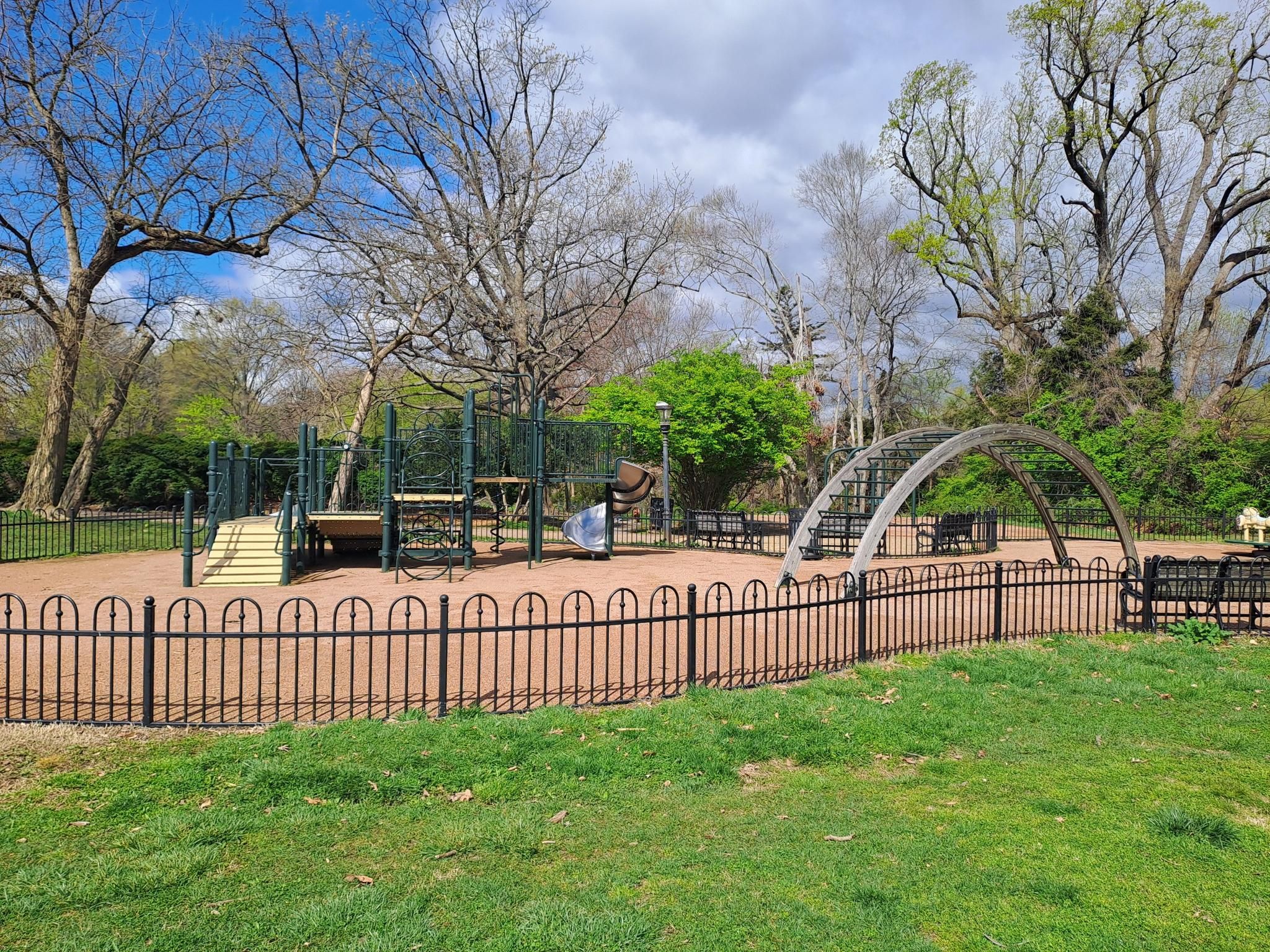 An empty playground with metal structures and a fence, surrounded by trees. - Dumbarton Oaks and Montrose Ropewalk