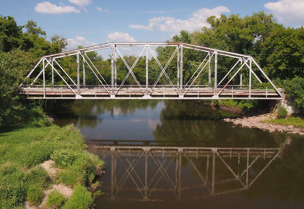 White metal truss bridge spanning a river, reflecting in water, under a sunny sky. - Waterford to Chub Lake Wildlife Management Area gravel loop