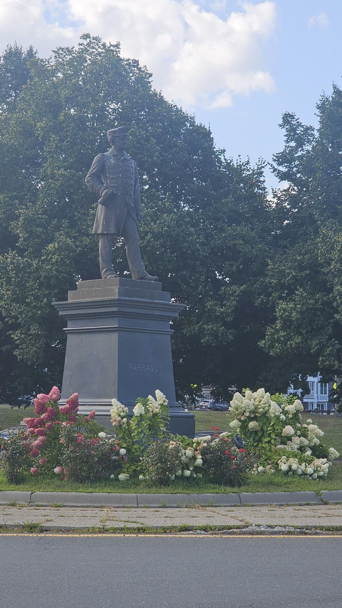 Statue of a man on a pedestal, surrounded by colorful flowers and trees.
