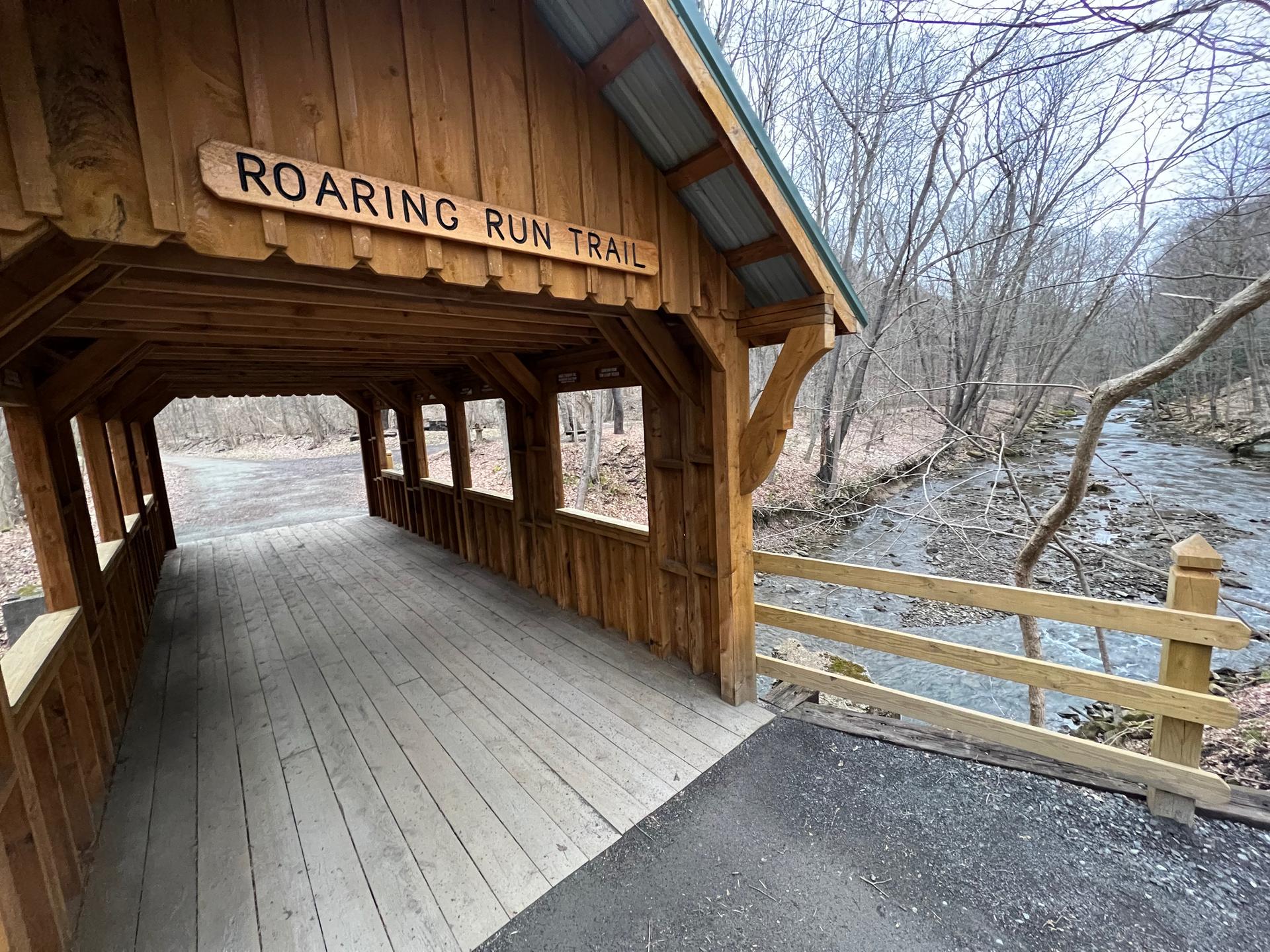 A wooden covered bridge spans a stream, surrounded by bare trees under diffused light.