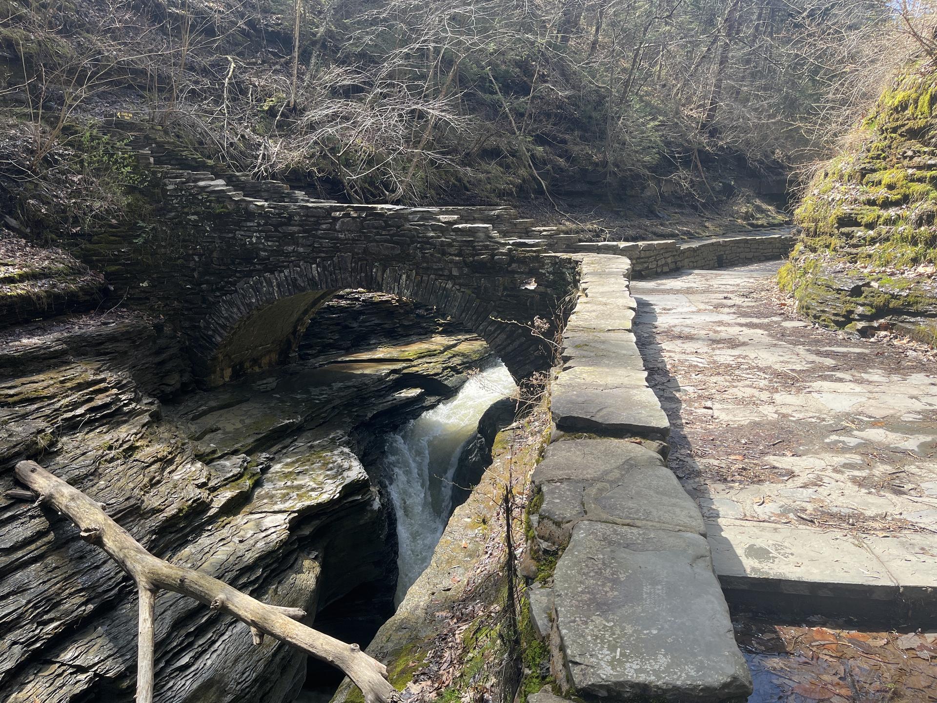 Stone bridge over a narrow gorge with flowing water, sunny day.