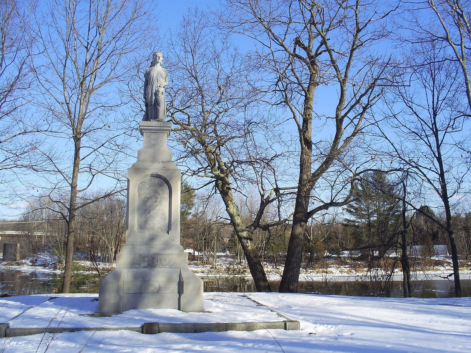 Stone monument with a statue on a snowy, bright winter day.