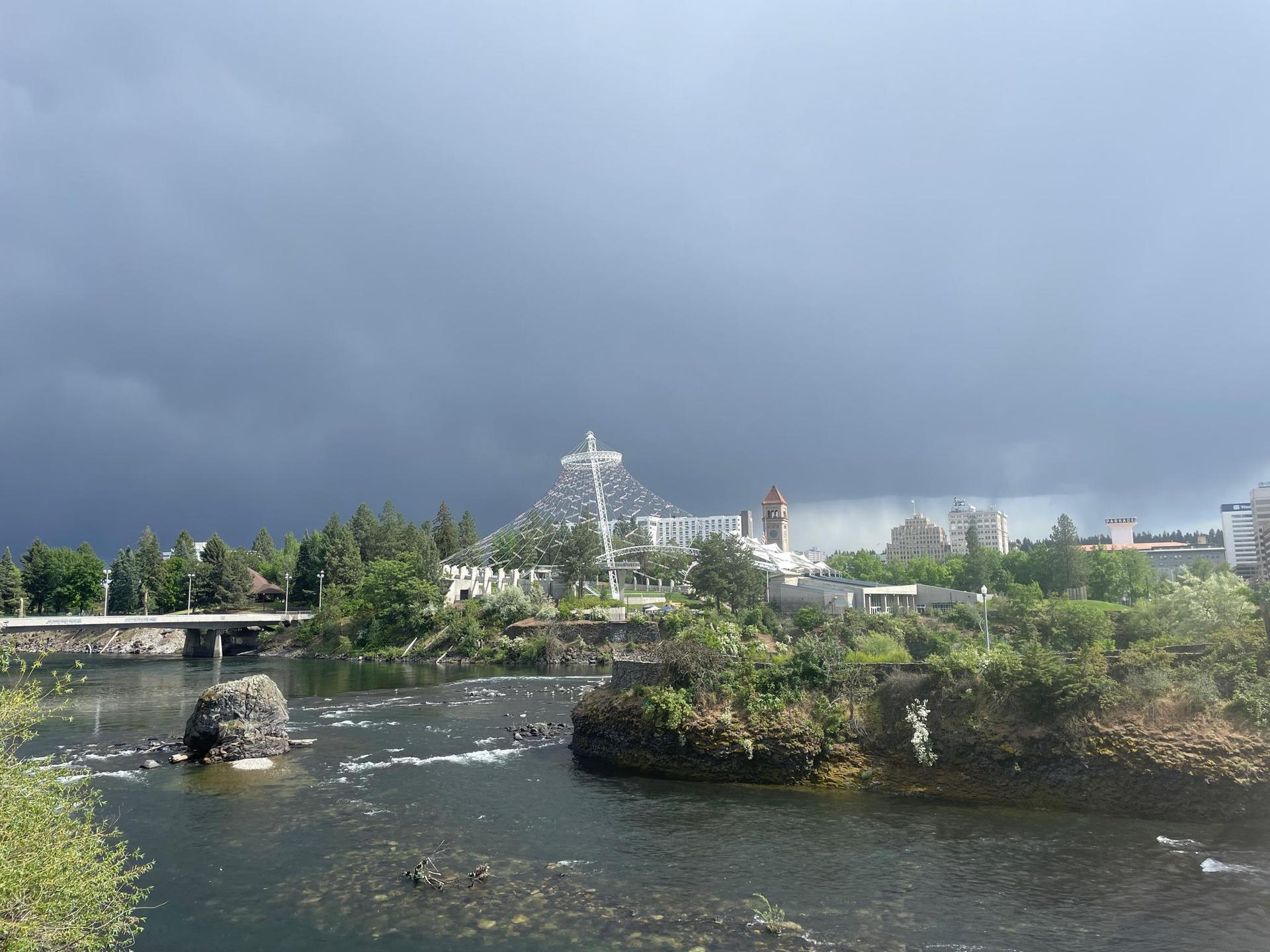 River flowing under a bridge, with a large glass structure under a stormy sky.