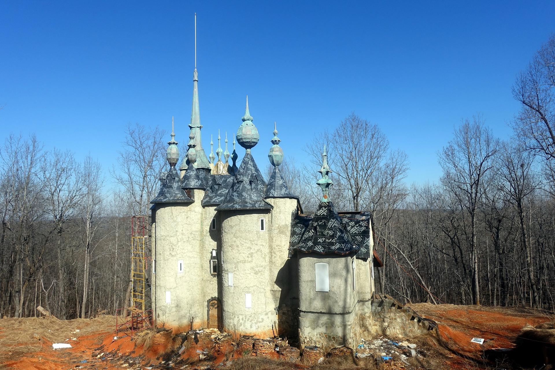 A whimsical, spired castle stands on a dirt mound under a clear blue sky.