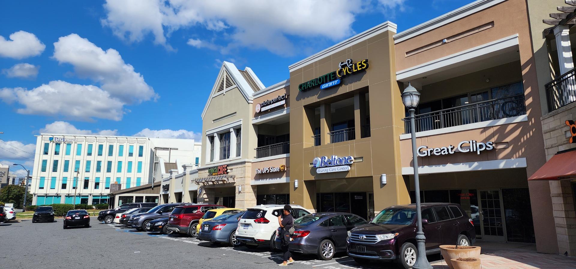 A row of commercial buildings with shops and parked cars under a blue sky.