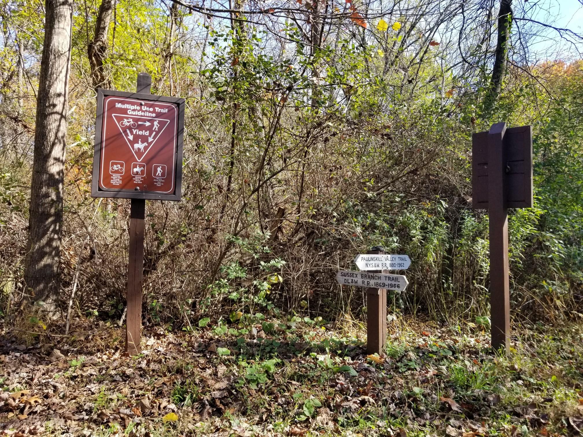Two trail signs stand at a path junction in a sunlit forest. - Warbasse Junction loop from Lafayette Township
