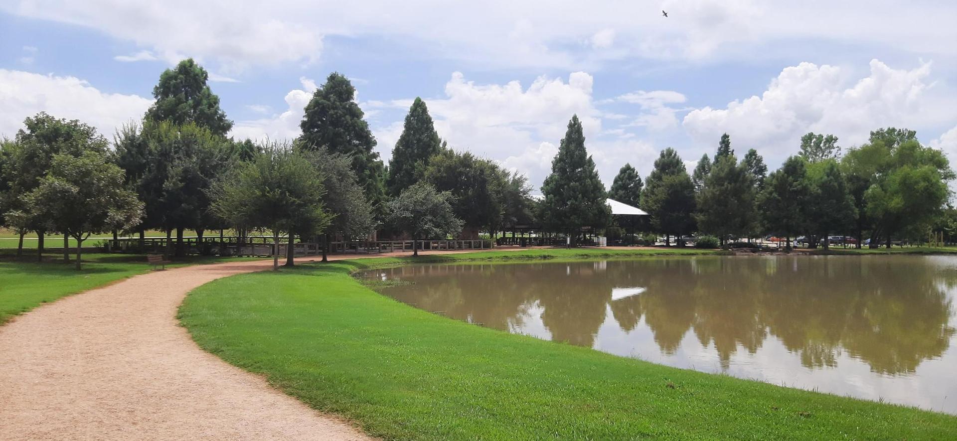 Winding dirt path next to a calm lake, green grass, and trees.