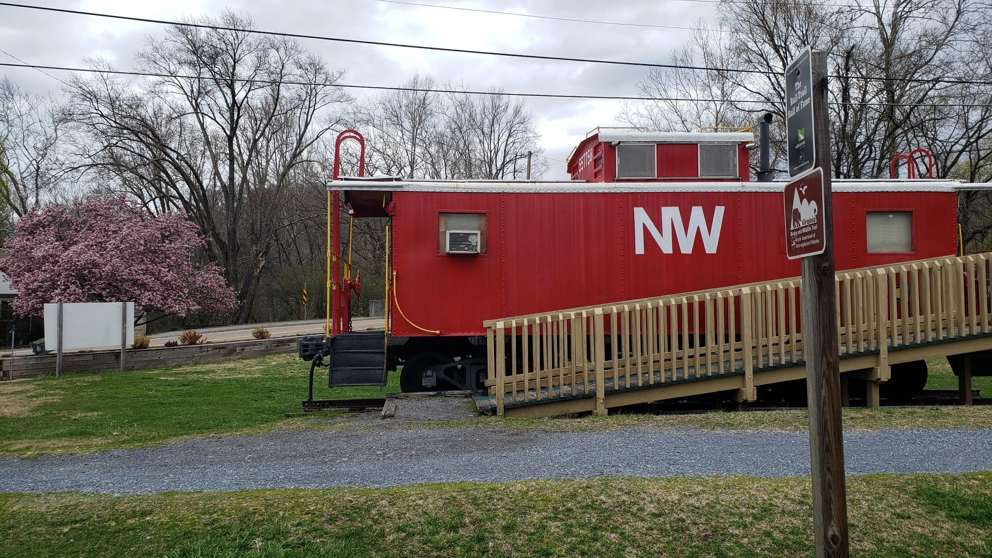 A red train caboose with a wooden ramp sits beside a gravel path.