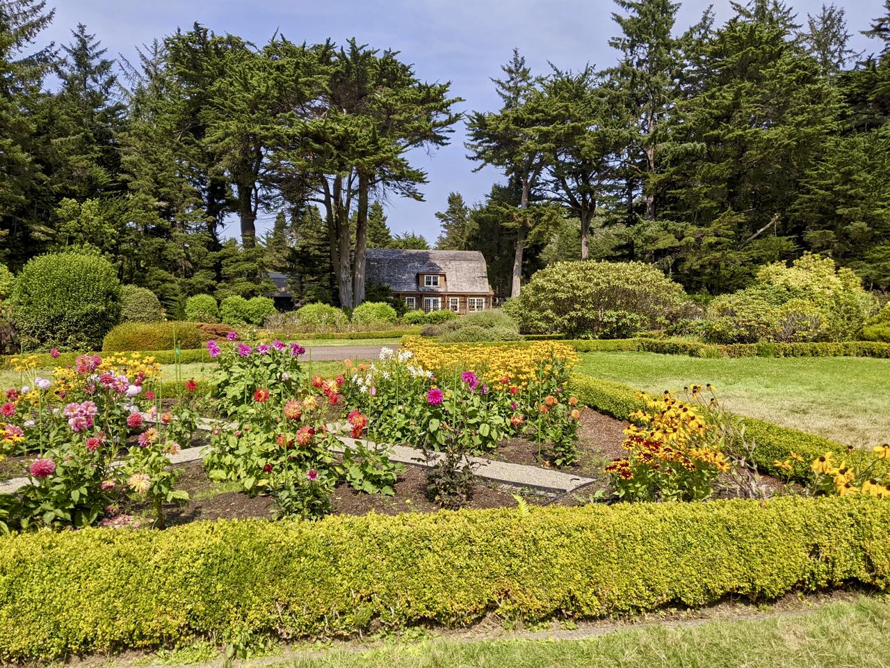 Vibrant flower garden with manicured hedges, green lawn, and a house under sunny skies.