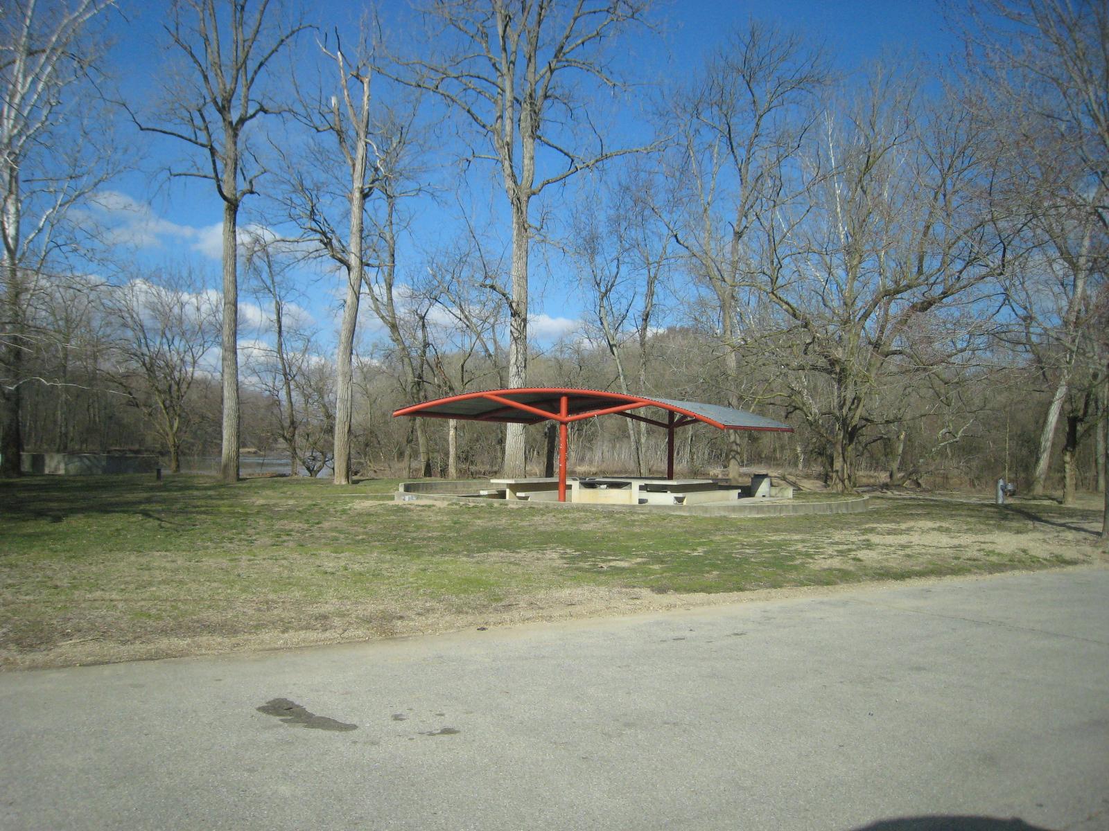 A red-roofed picnic shelter stands in a grassy area with bare trees.