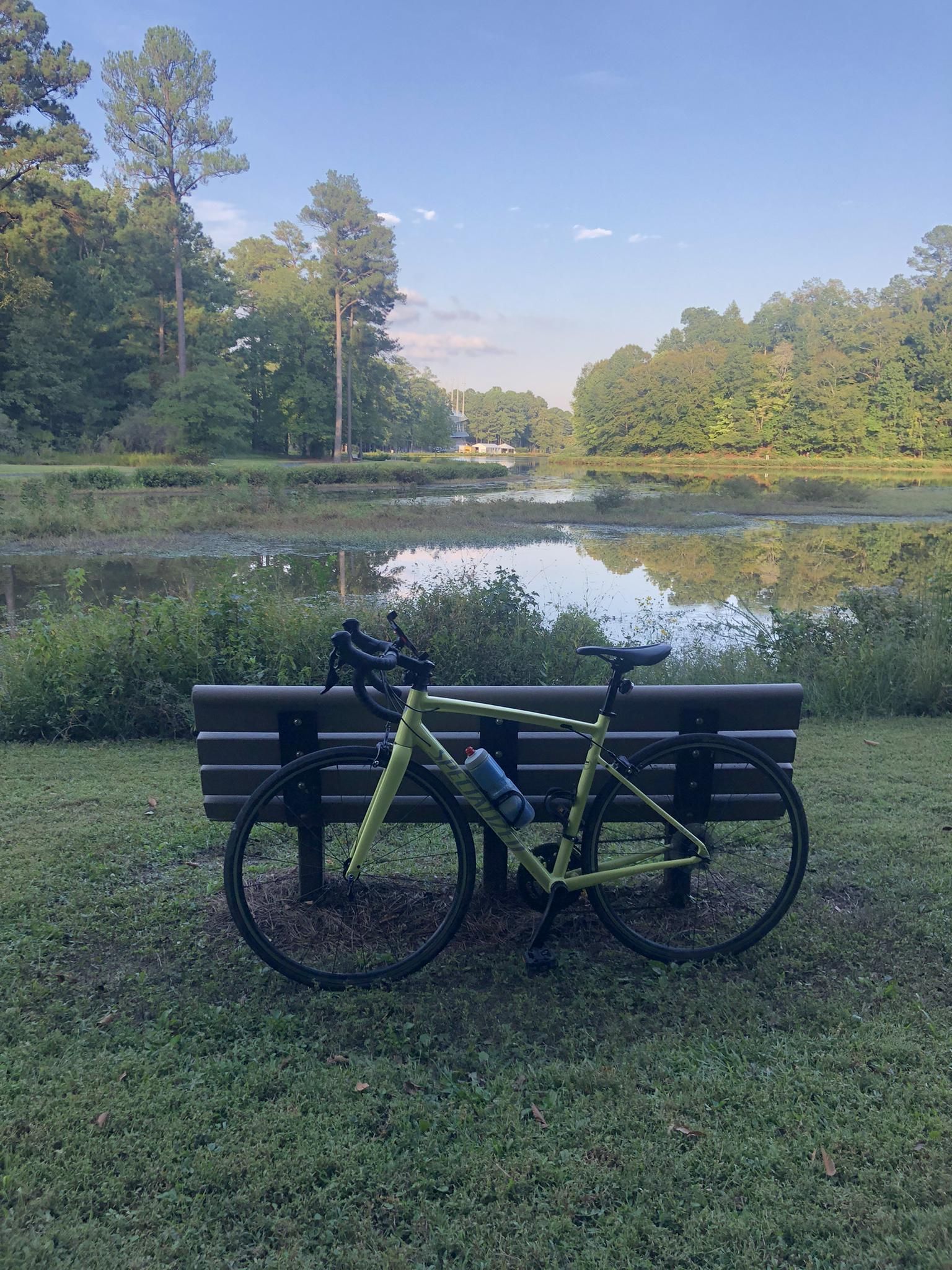 A lime green bicycle rests against a bench by a tranquil lake. - Symphony Lake – Harris Lake loop from Kelly Glen Park