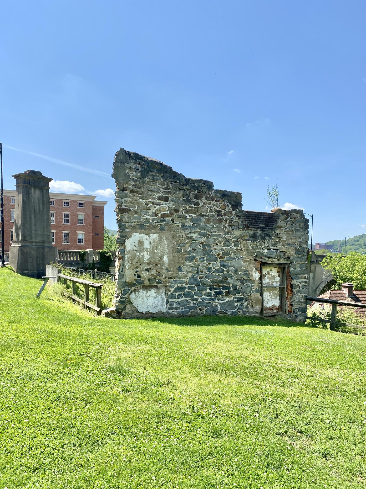 Stone ruins of a building on a grassy hill under a clear blue sky.