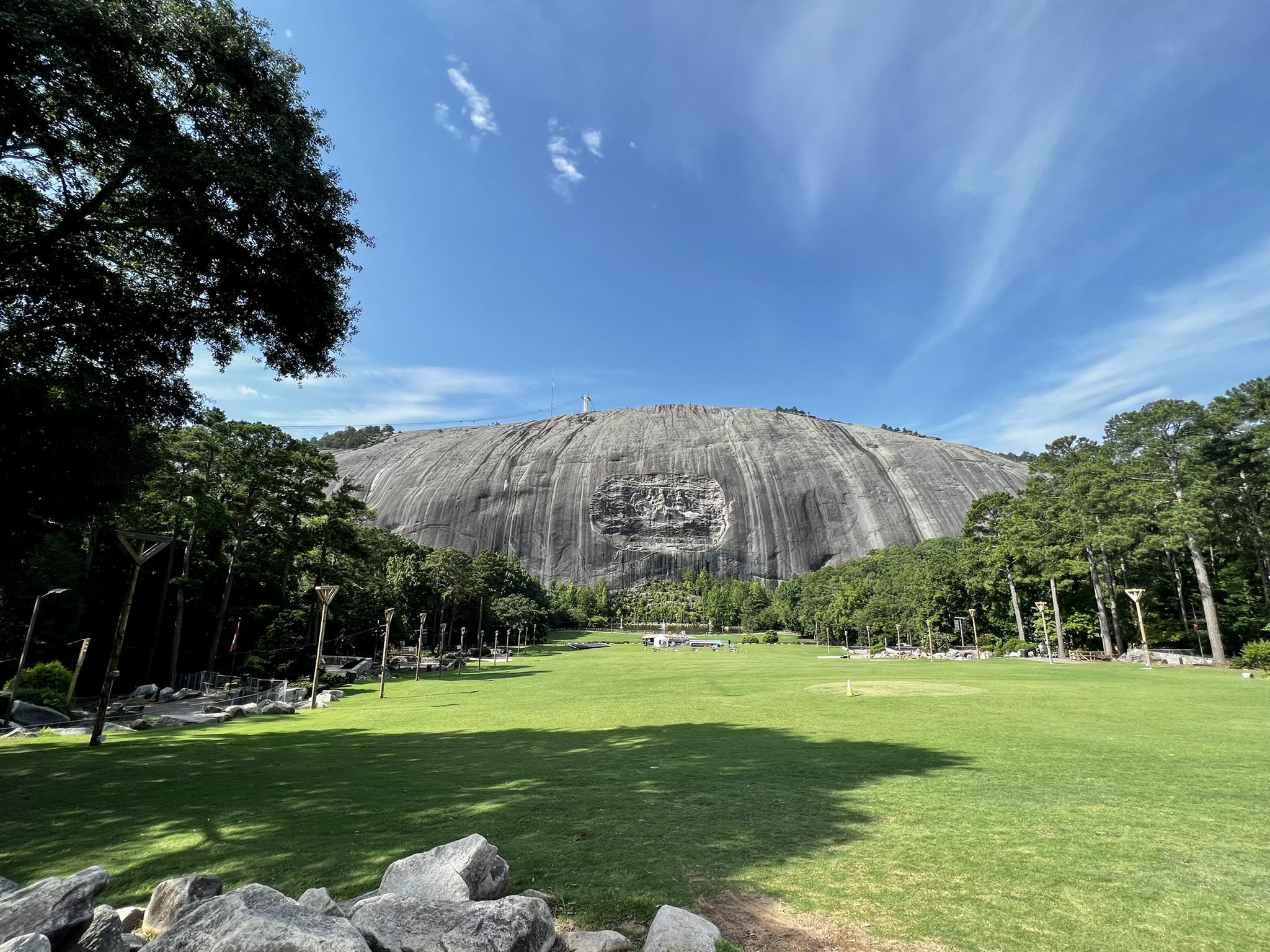 Huge gray rock mountain with carvings overlooking a wide green lawn.