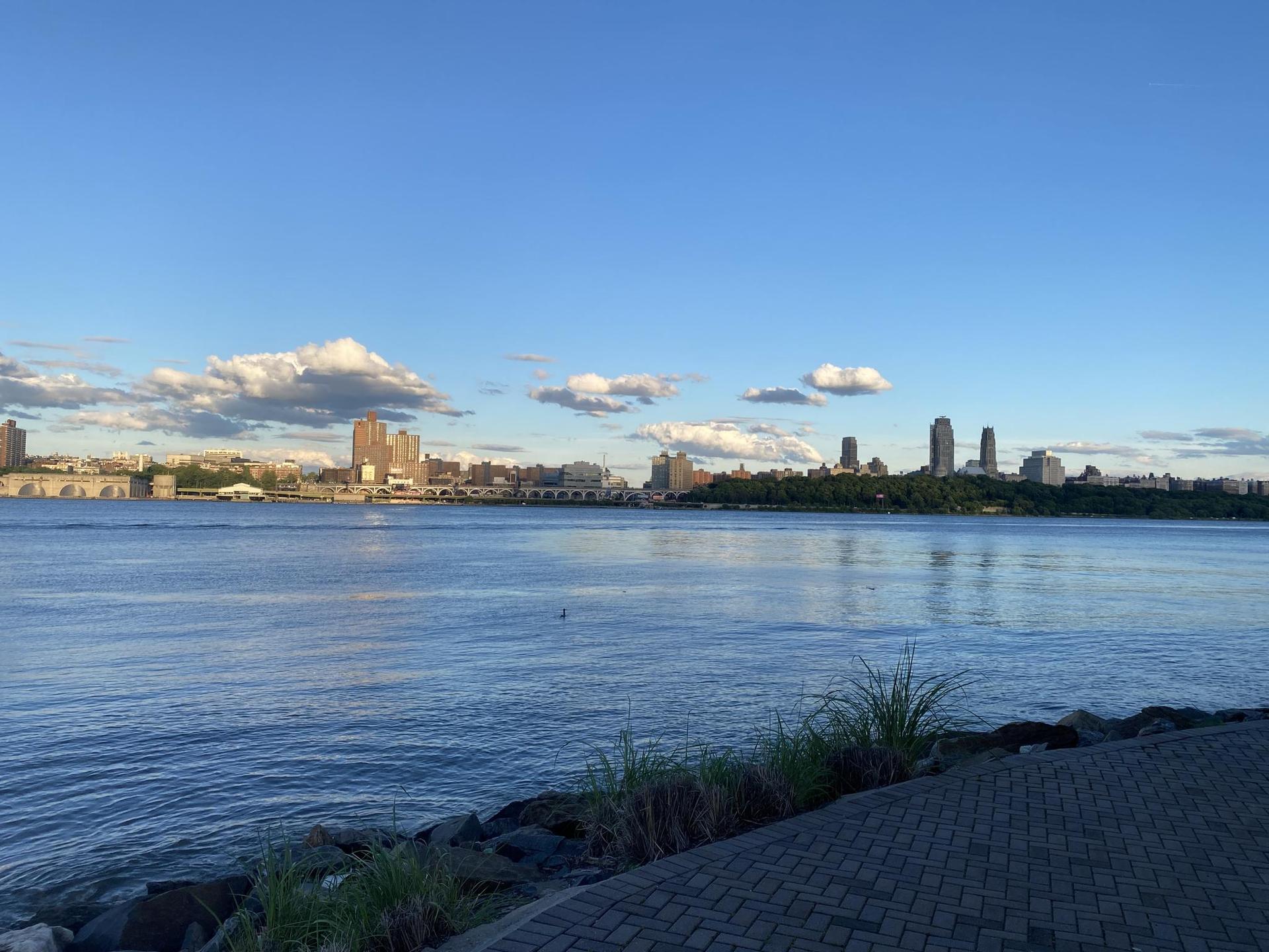 Calm river with a distant city skyline under a bright blue sky.