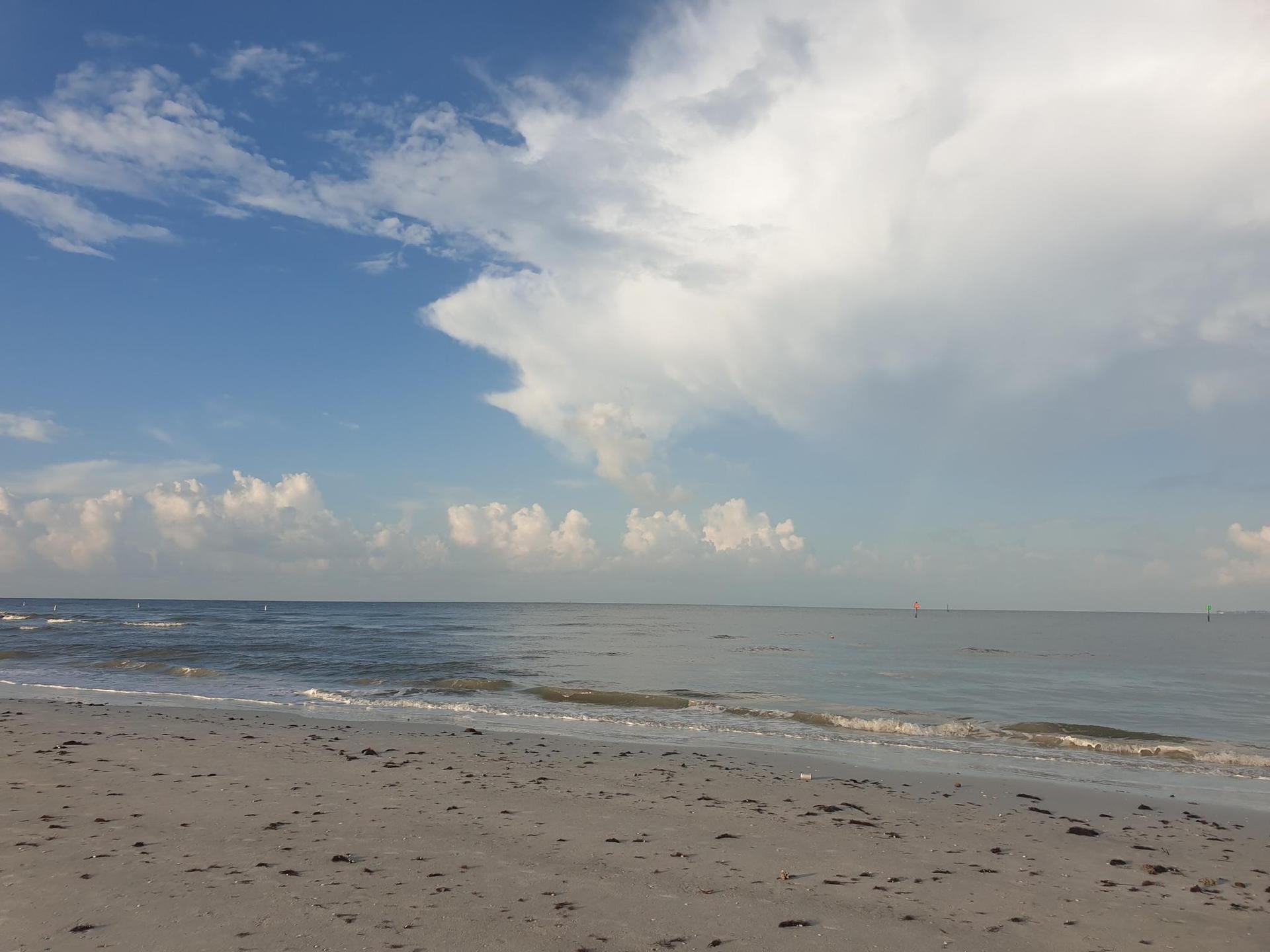Sandy beach with gentle waves meeting the shore under a partly cloudy sky.