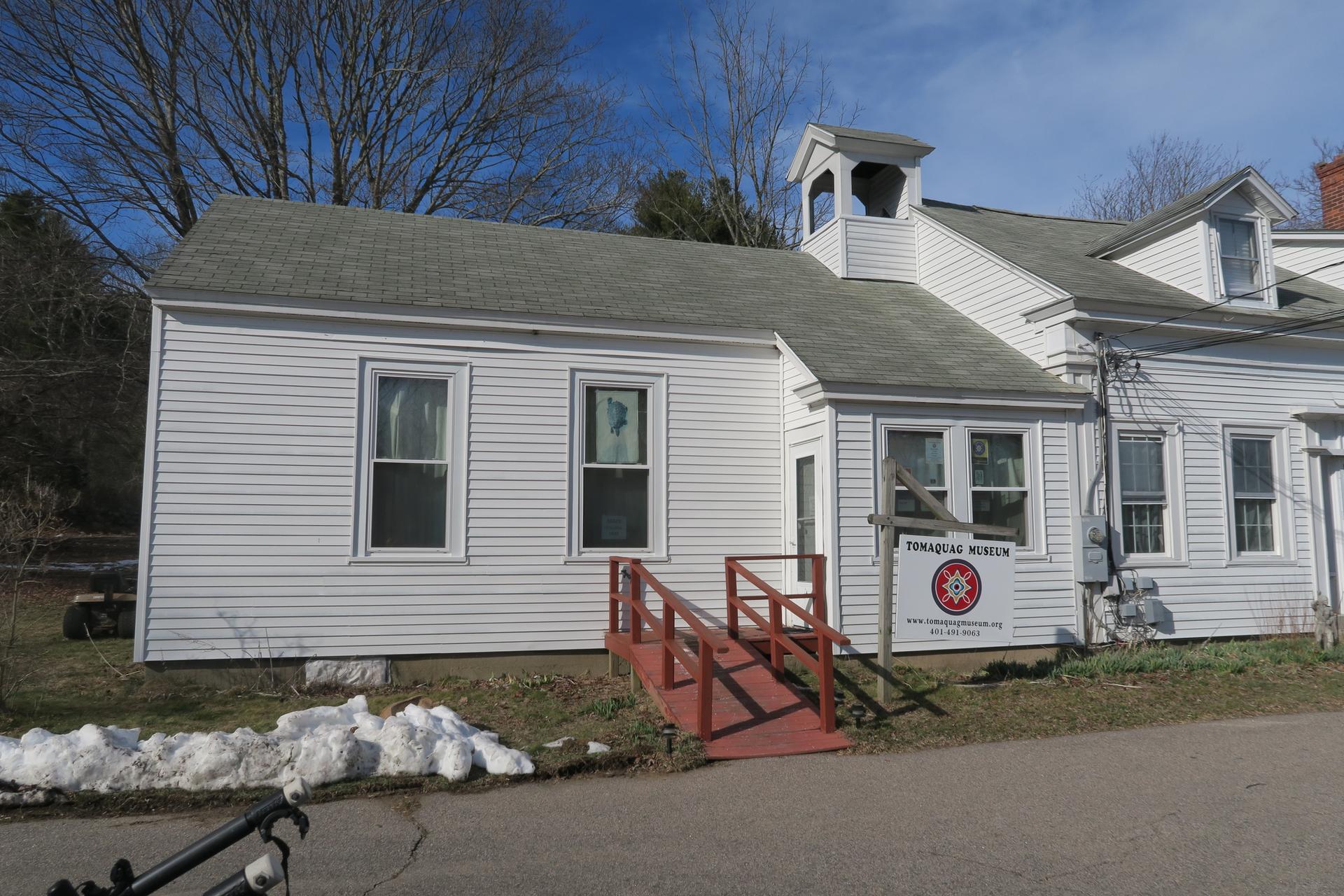 White clapboard building with cupola, red ramp, and snow patches under blue sky.