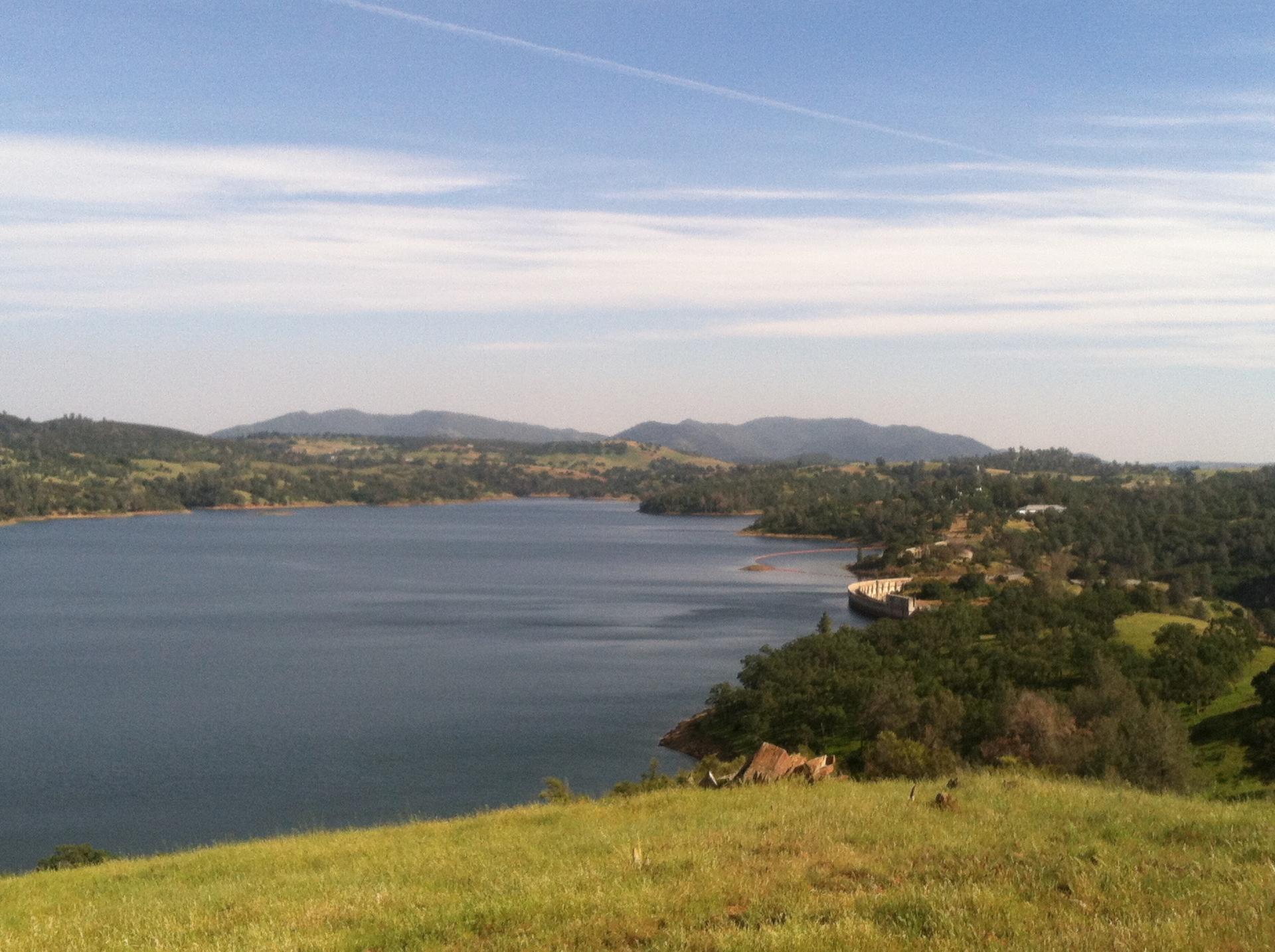 Expansive lake surrounded by rolling hills under a bright, clear sky.