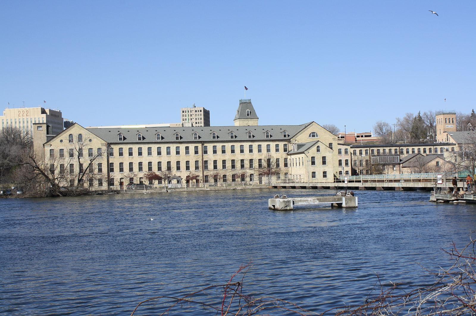 Large historic building with a clock tower next to a wide river.