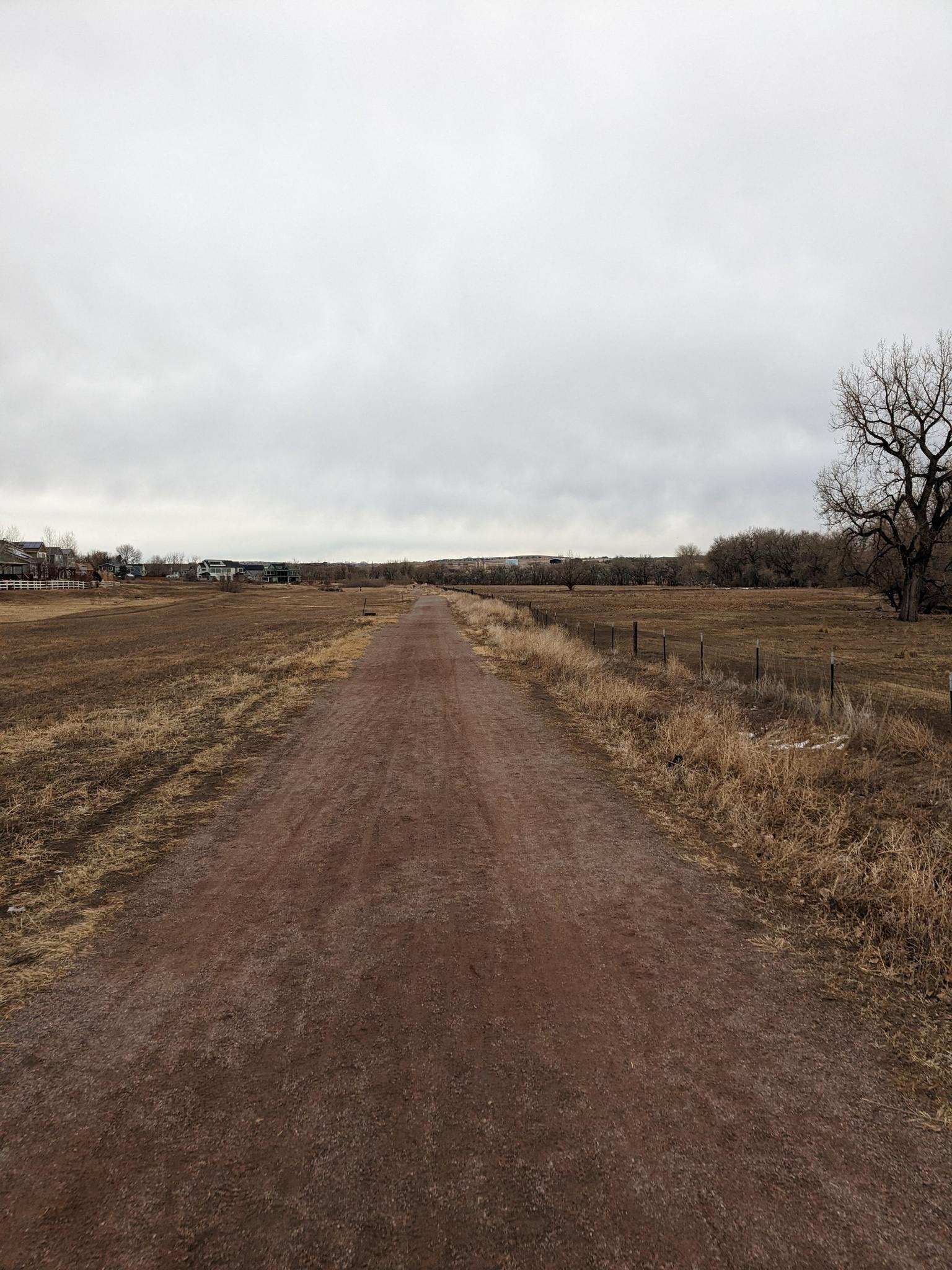 A long dirt path extends through brown fields under an overcast sky.
