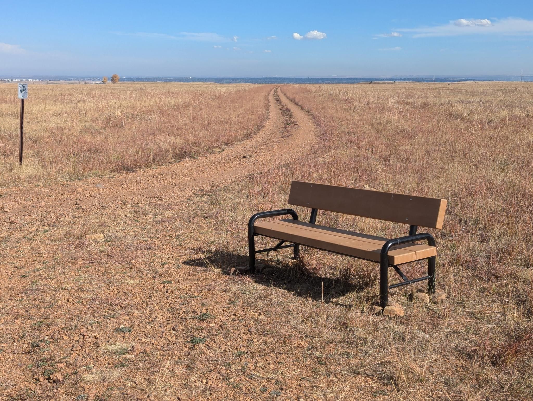 A wooden bench sits beside a winding dirt path through dry golden fields. - Greenway Trail View – Outhouse! loop from Rocky Flats National Wildlife Refuge trailhead