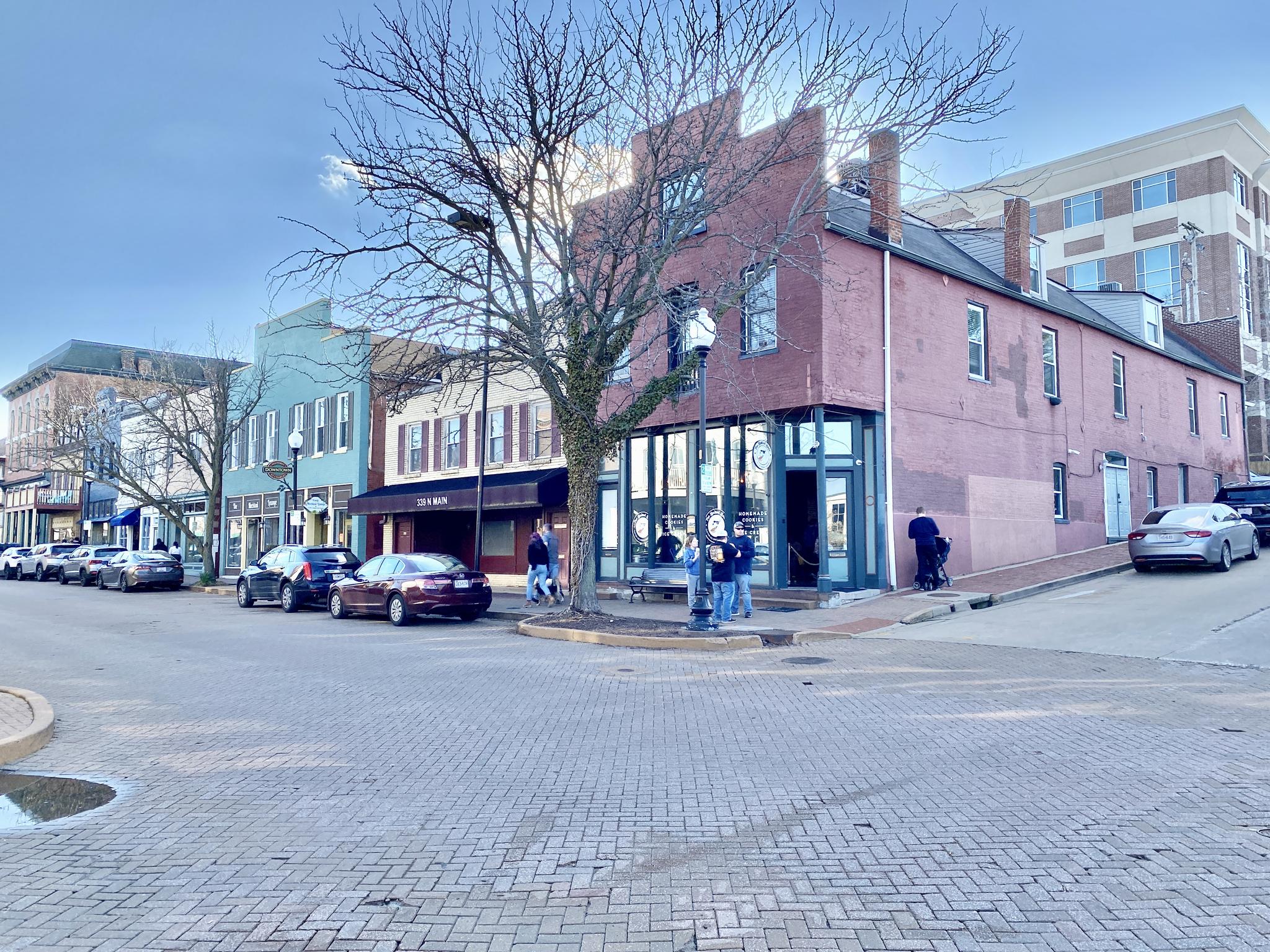 Historic brick buildings line a street with parked cars and pedestrians.