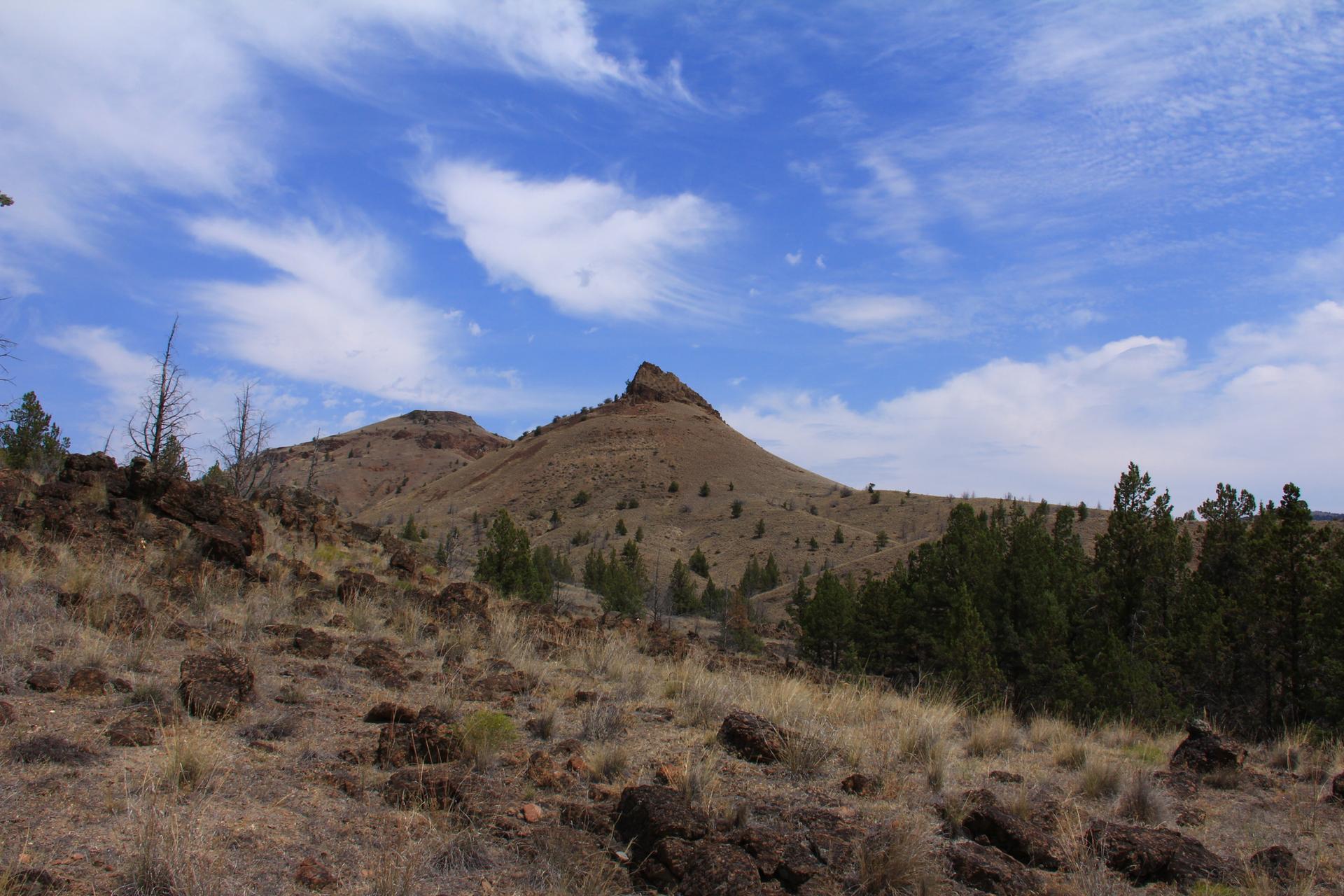Rocky foreground leads to a pointed hill under a bright, cloudy sky.
