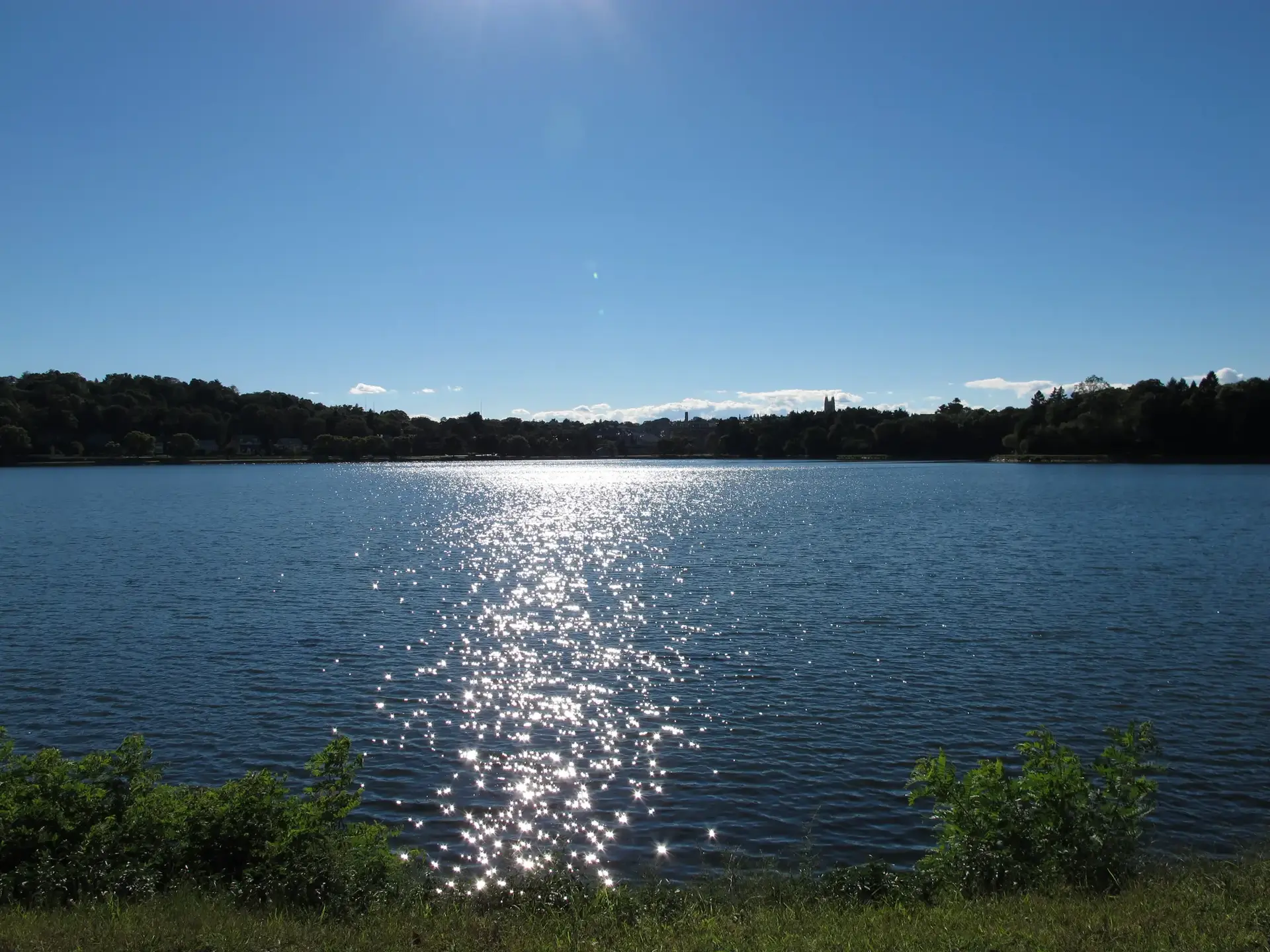 Bright sun glinting on a wide lake under a clear blue sky.