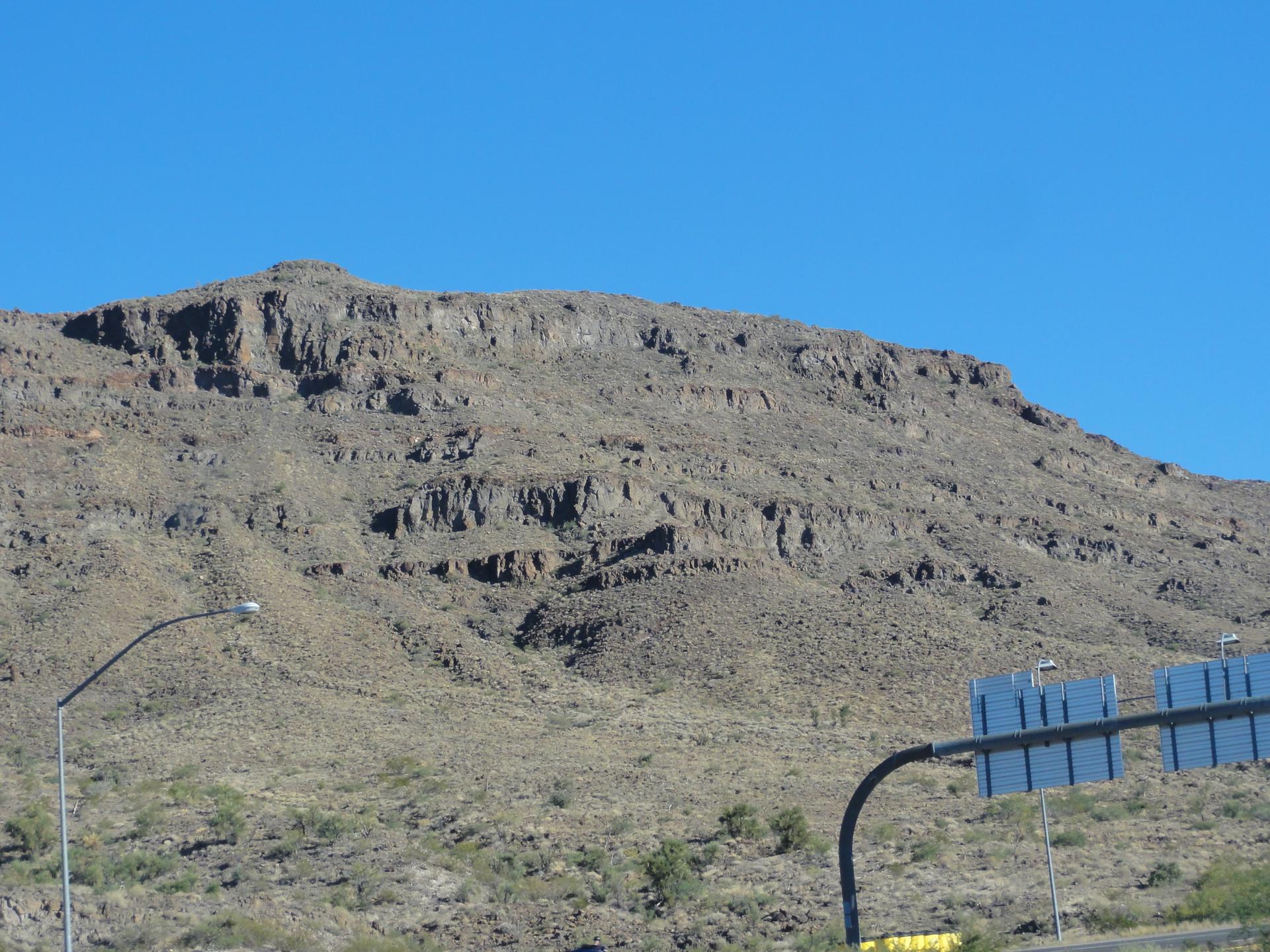 Steep, rocky desert mountain with road signs and a street light.