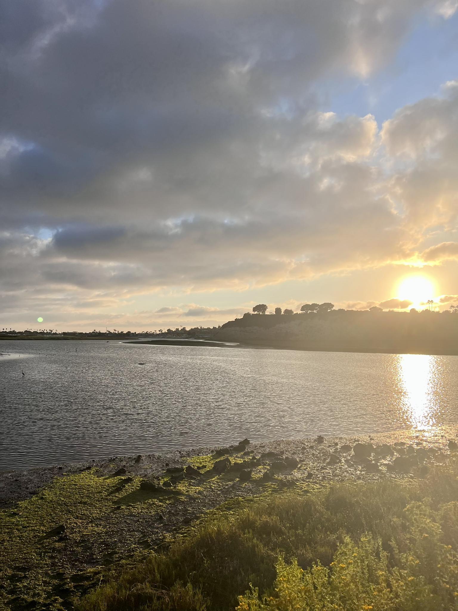 Golden sunset over a calm body of water with cloudy skies.