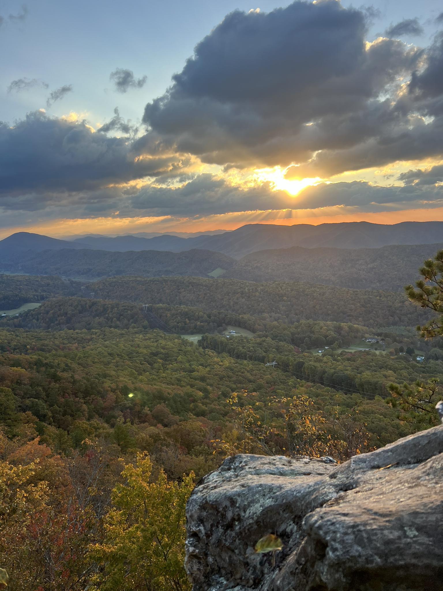 Golden sunset over a vast forest and distant mountains, with dramatic clouds.