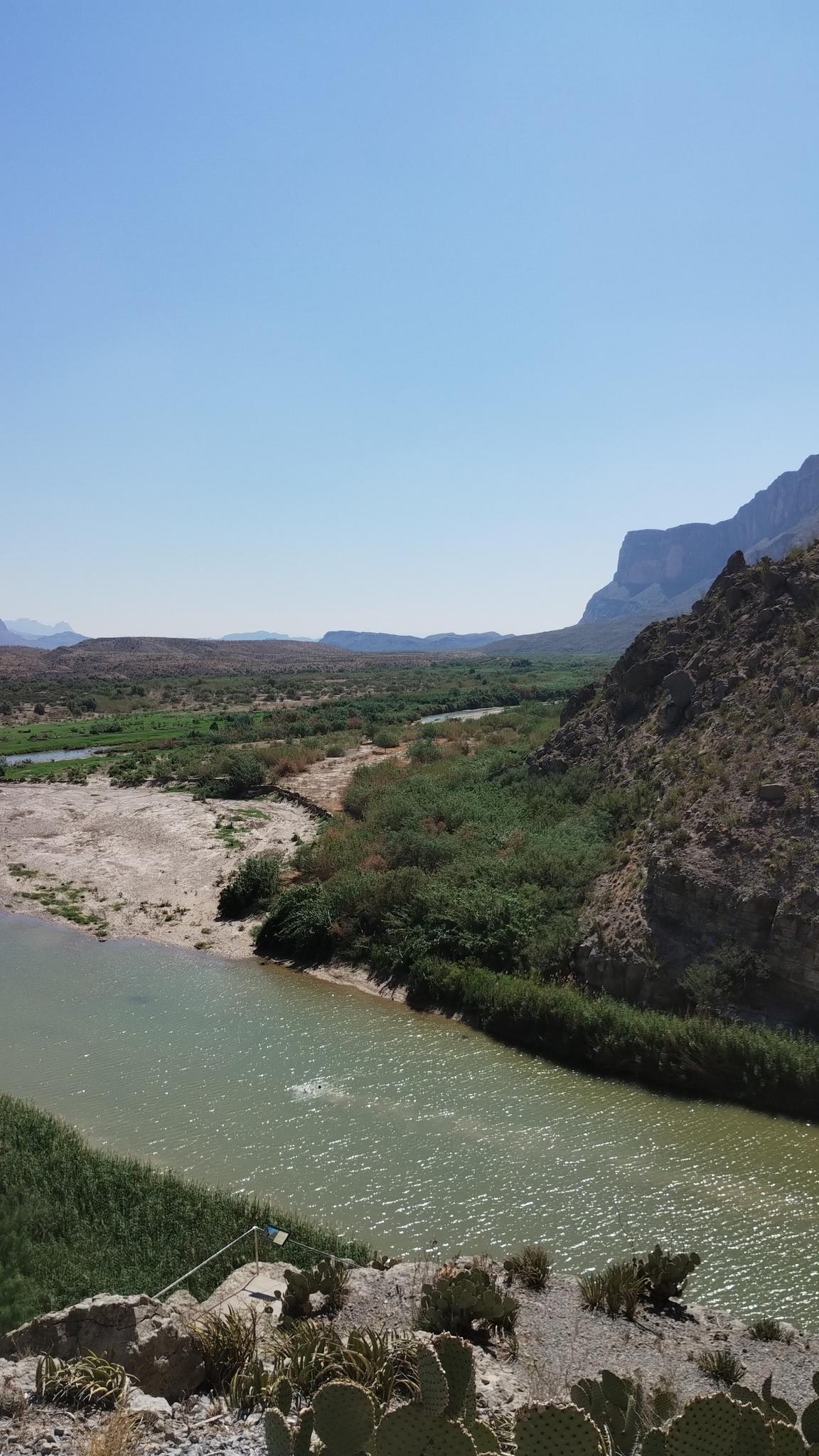 River flowing through a desert canyon with green vegetation under clear blue sky.
