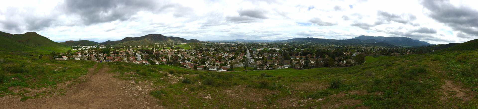 Panoramic view of a town nestled in green hills under a cloudy sky.