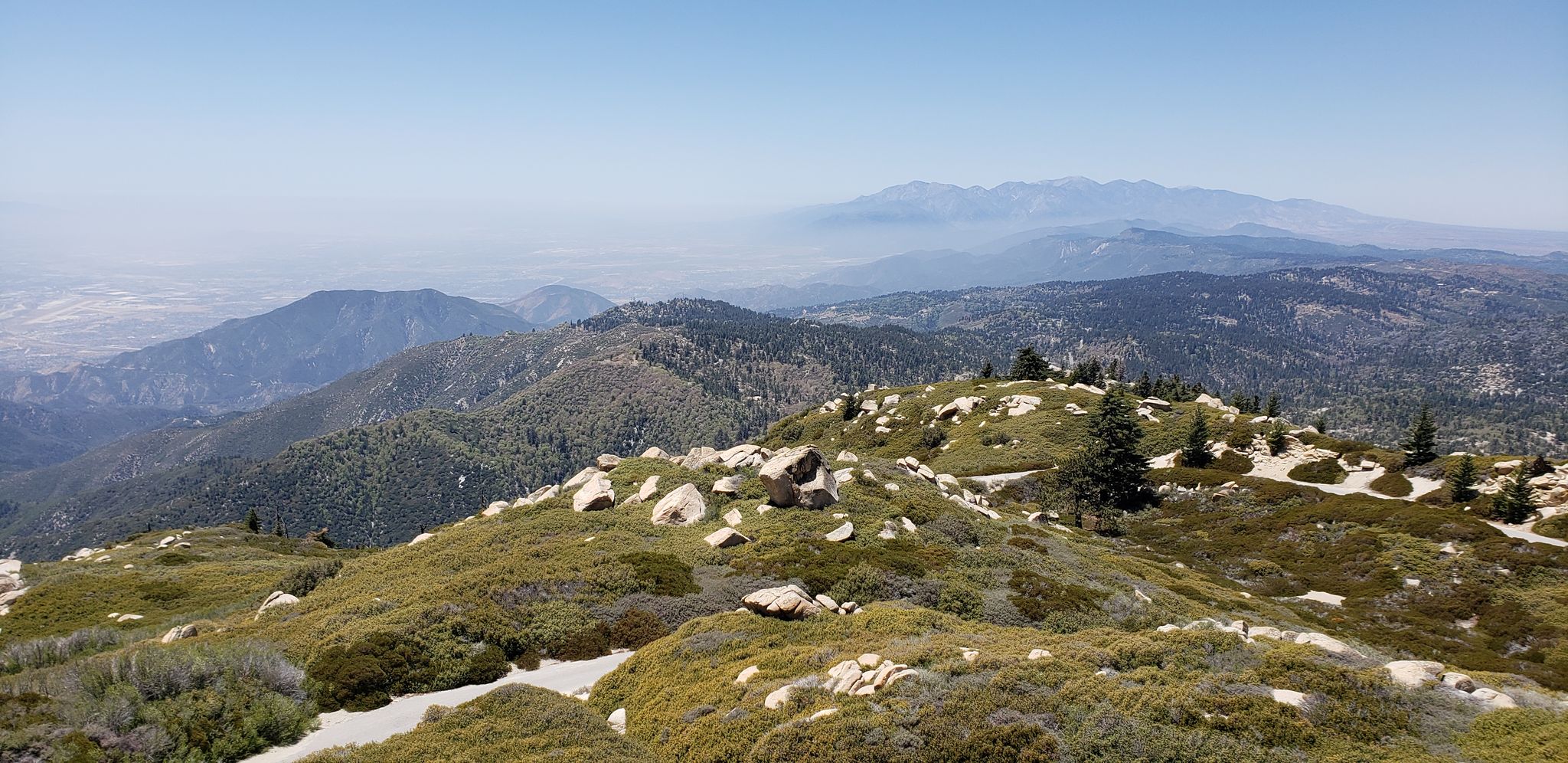 Rocky, shrub-covered mountain peak overlooking a vast, hazy valley under clear skies. - Keller Peak via Exploration Trail